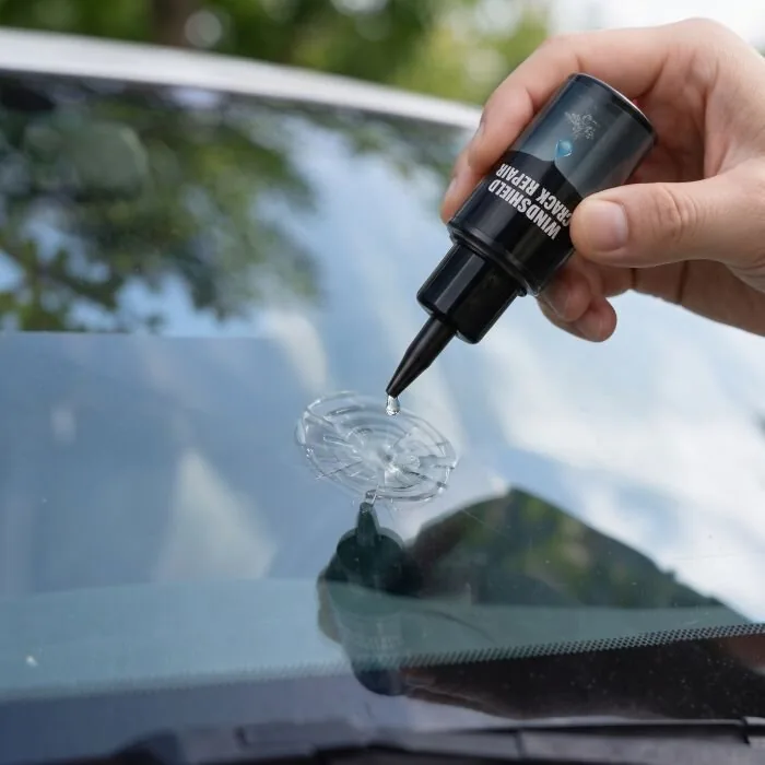 Hand holding the Glasyx bottle over a windshield chip with a drop of resin on the glass